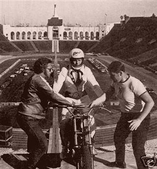 Two men assist Evel Knievel at the end of a ramp in the LA Coliseum