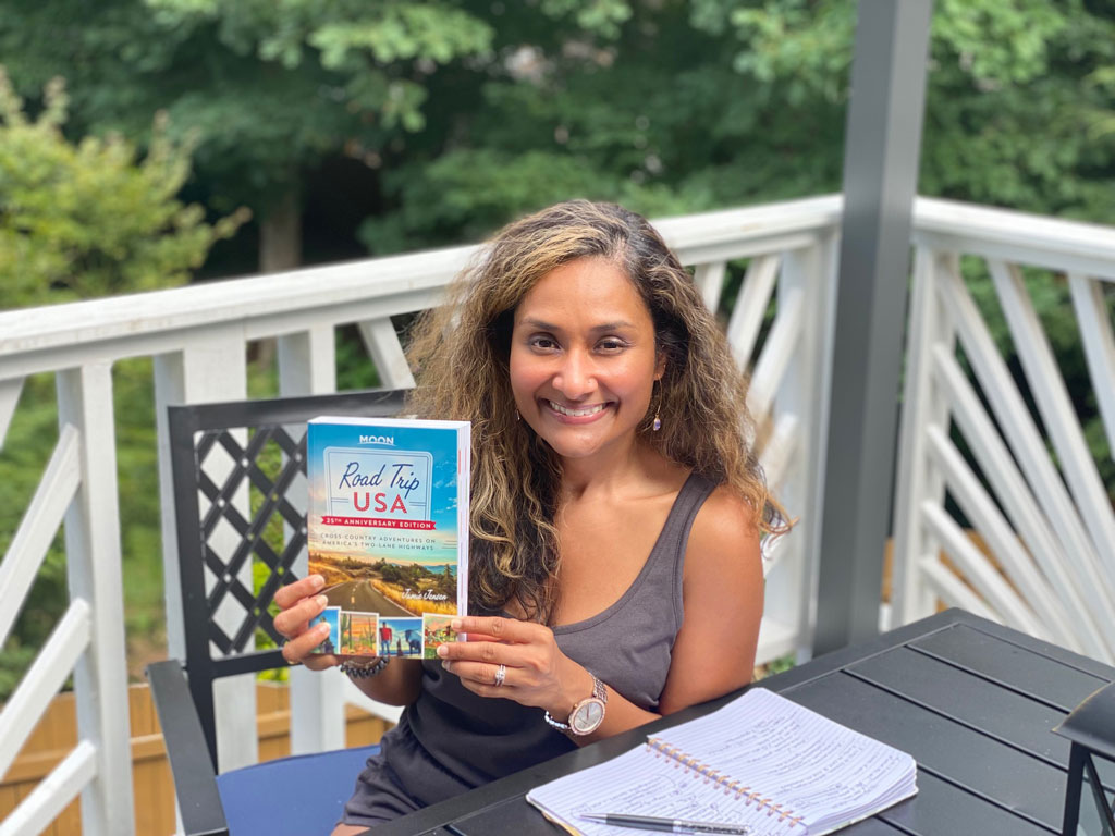 woman with medium brown complexion and long curly hair holding a road trip travel guide